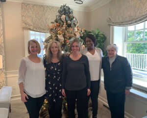 group of women standing in front of a christmas tree smiling